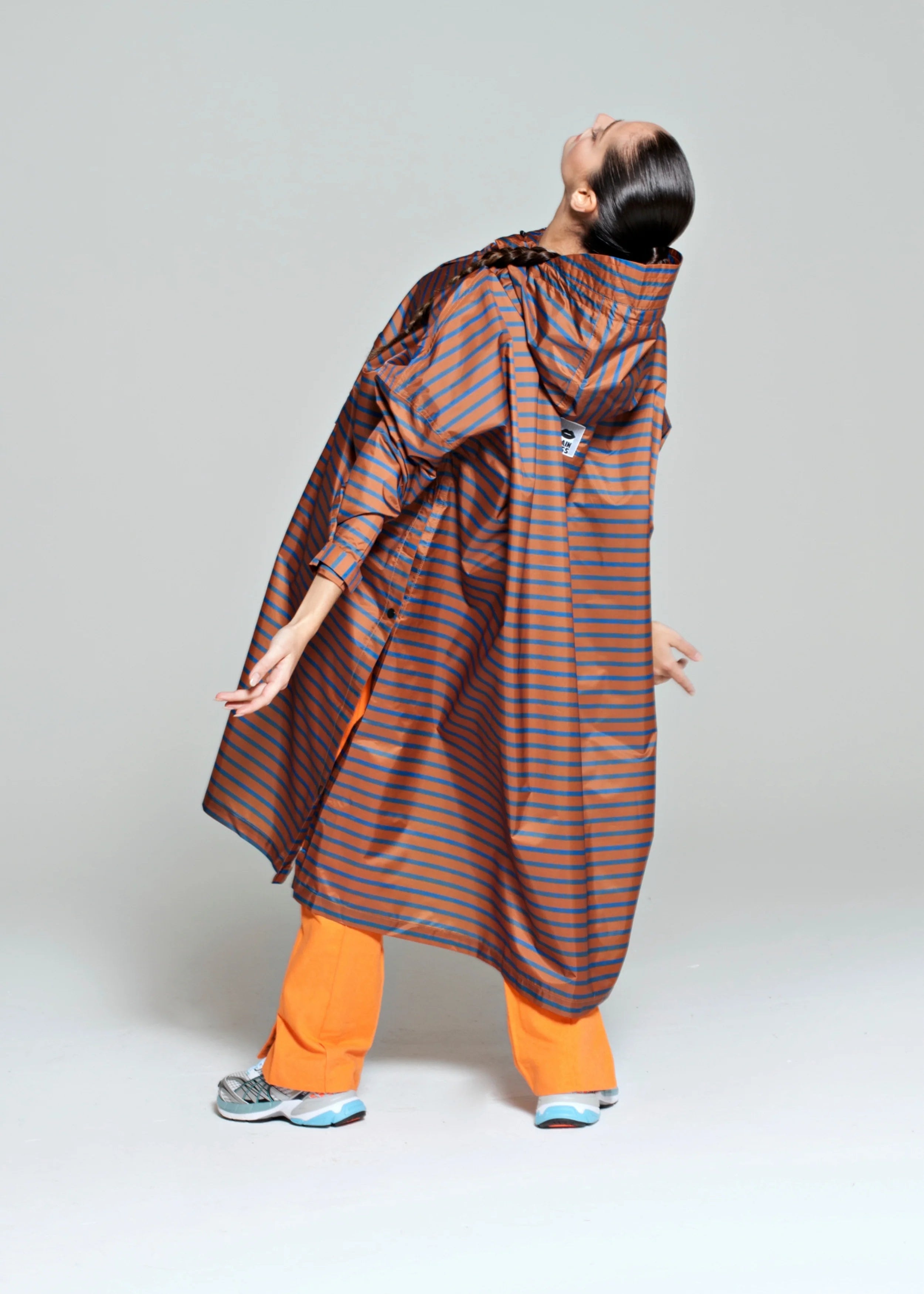 Person wearing a striped raincoat and orange pants on a plain background