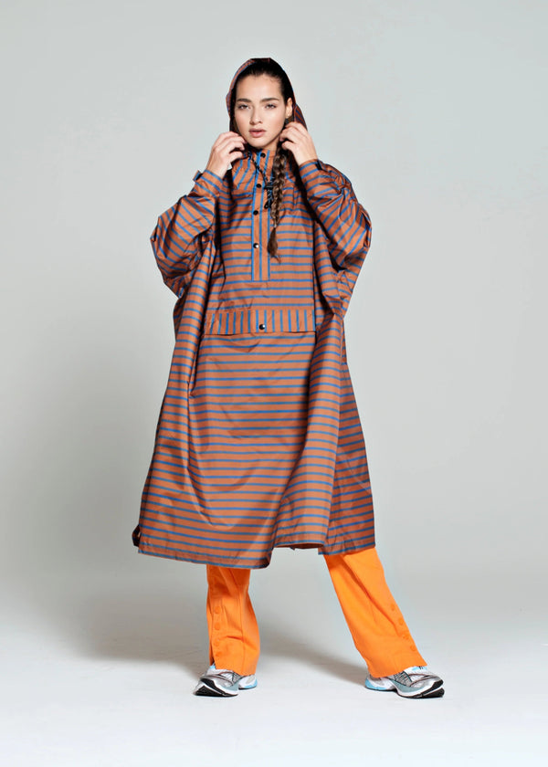 Person wearing a long, striped raincoat with orange pants on a plain background