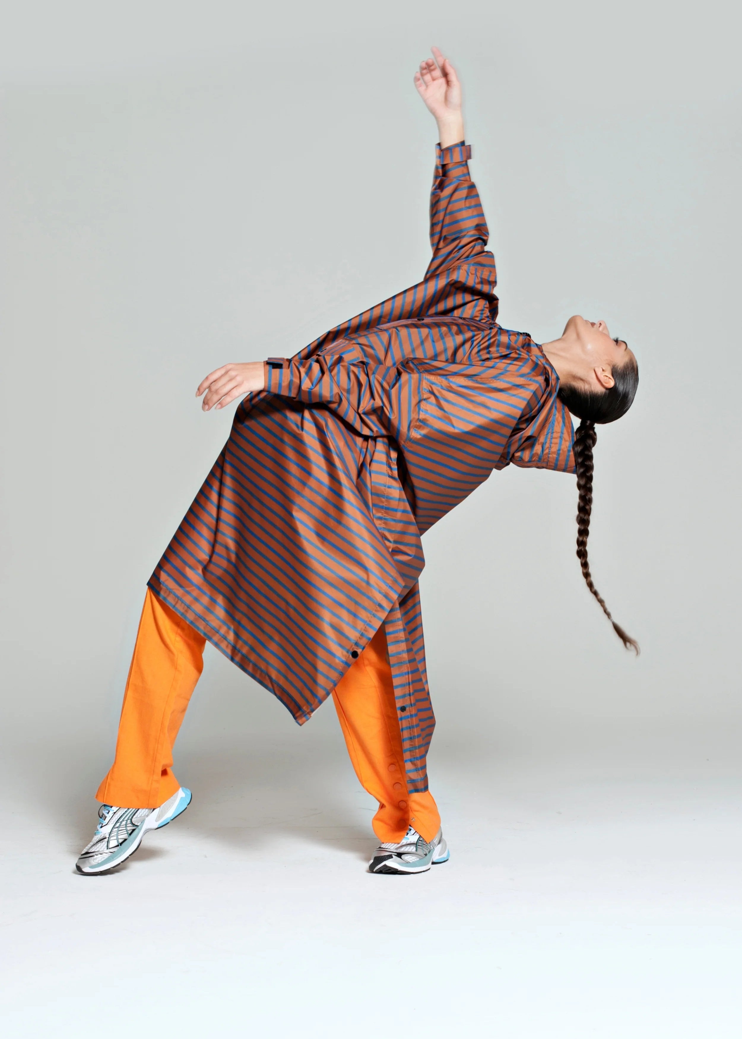 Person wearing a long, striped coat over orange pants on a plain background