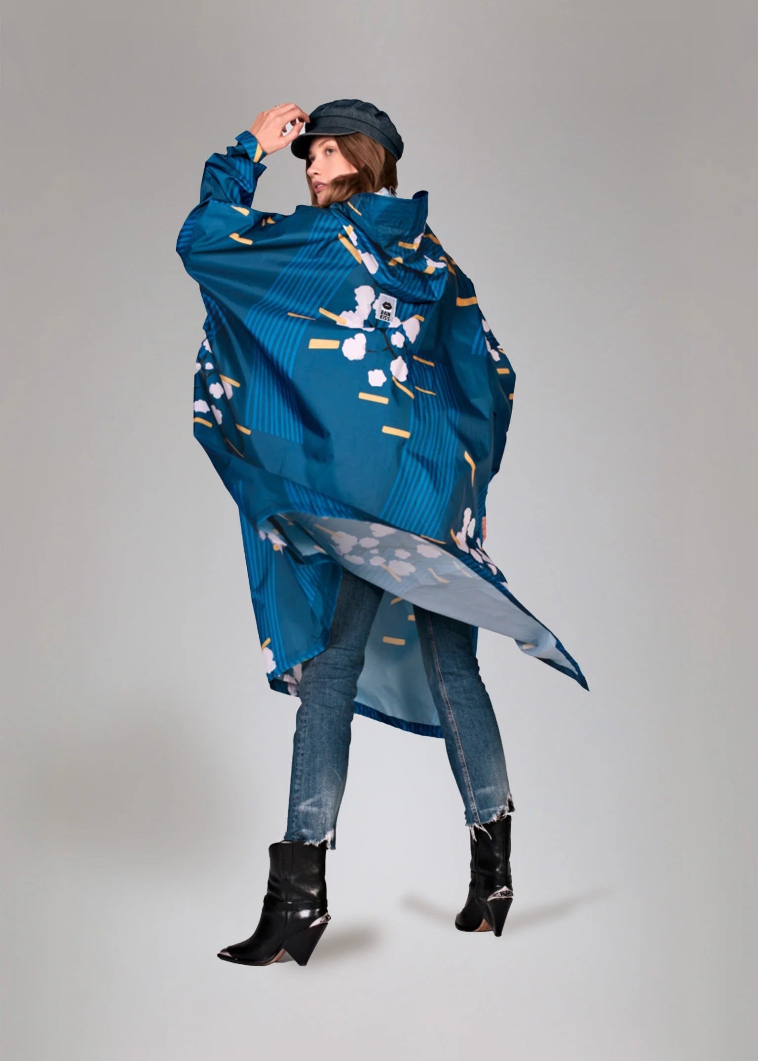 Person wearing a blue raincoat with floral pattern on a gray background