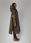 Person wearing a long olive green raincoat with a hood on a plain background