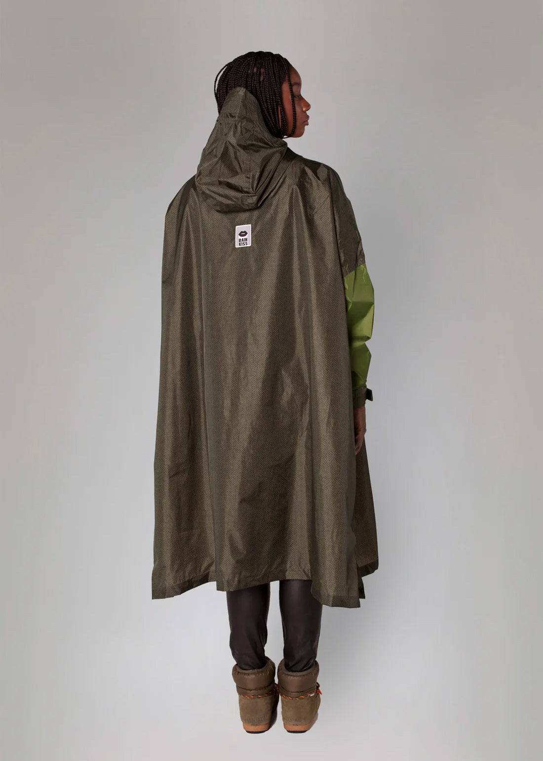 Person wearing a long olive green raincoat with a hood on a plain background