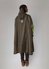 Person wearing a long olive green raincoat with a hood on a plain background
