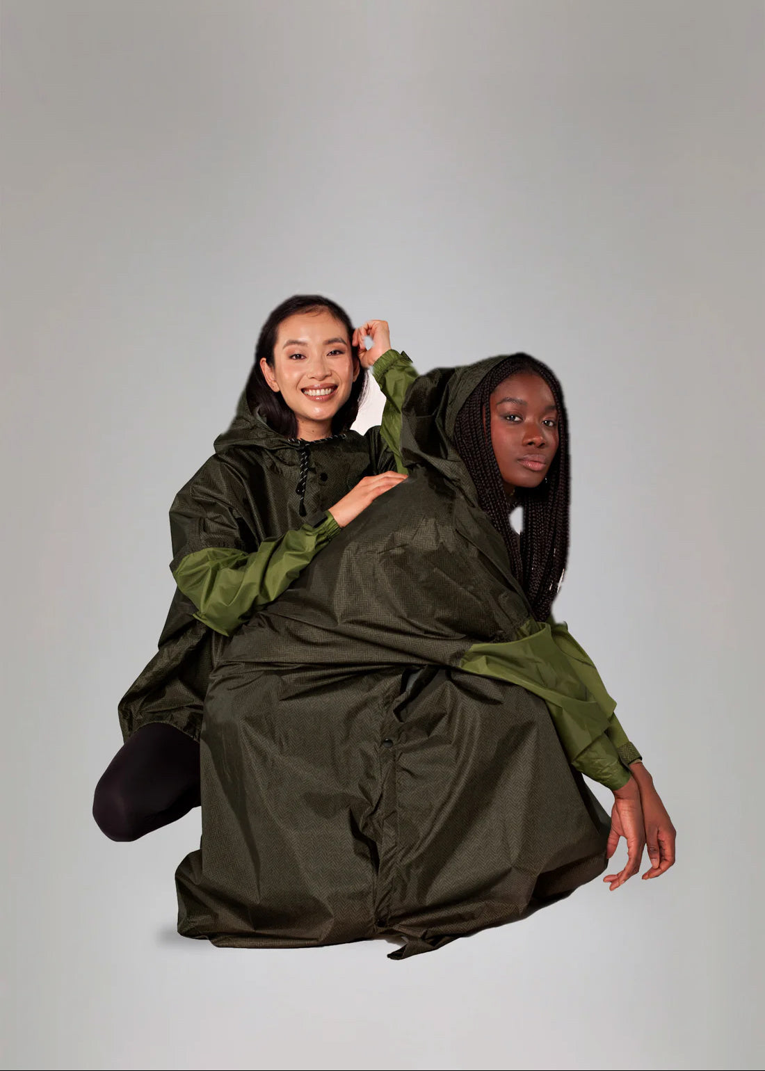Two people wearing a large green and black poncho against a plain background