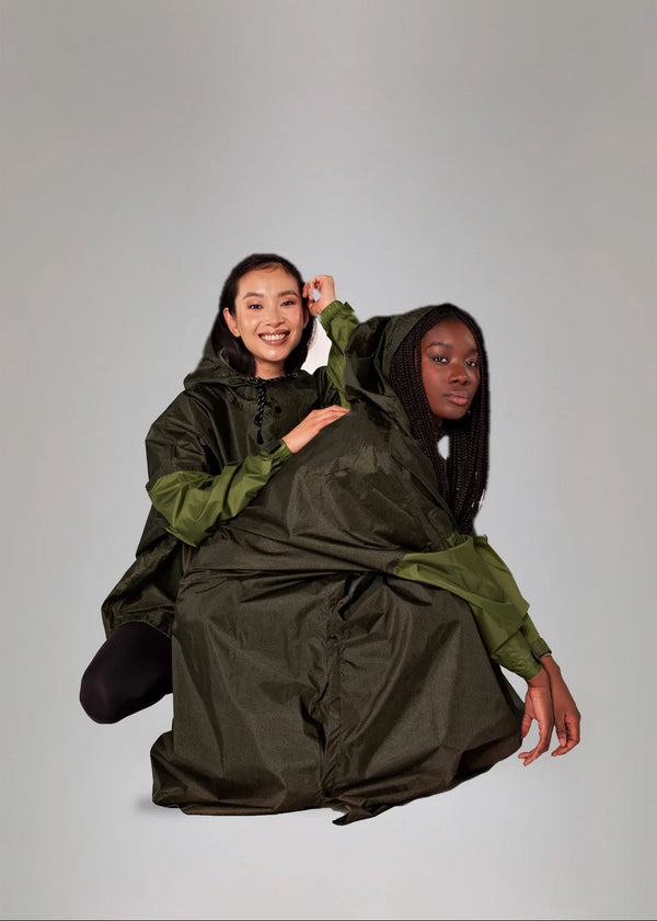 Two people wearing a large green and black poncho against a plain background
