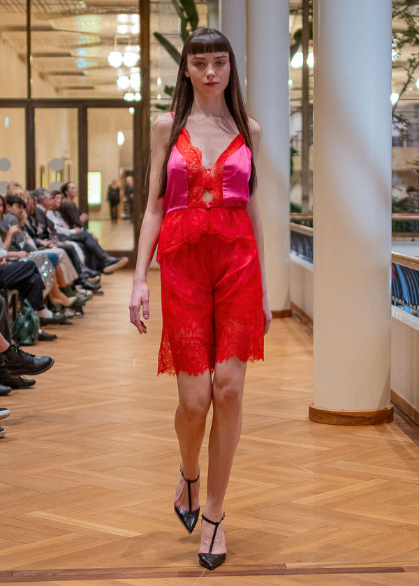 Model wearing a bright pink top and red lace shorts on a runway.
