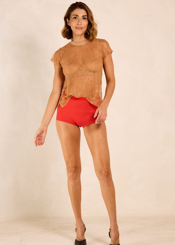 Woman wearing a brown top and red shorts on a beige background