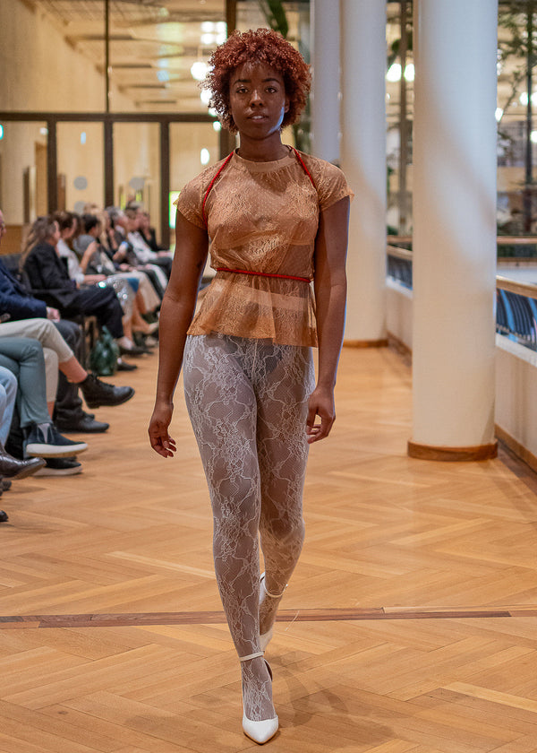 Model walking on a runway at a fashion event with a blurred indoor background