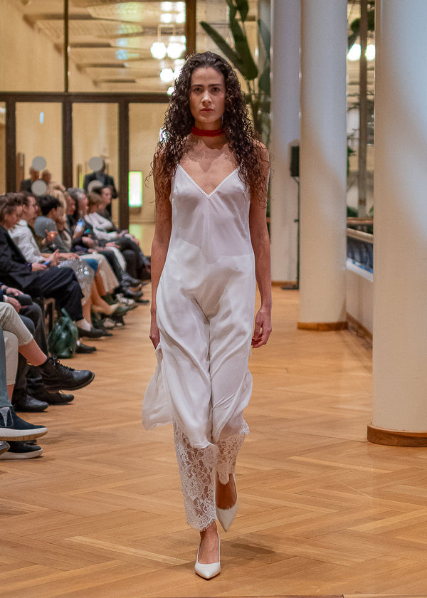 Model walking on a fashion show runway wearing a white outfit.