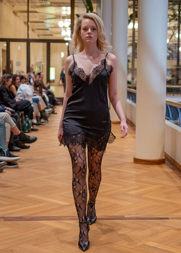 Model walking on a runway wearing a black lace dress and stockings at Zürich Fashion Week 2026.
